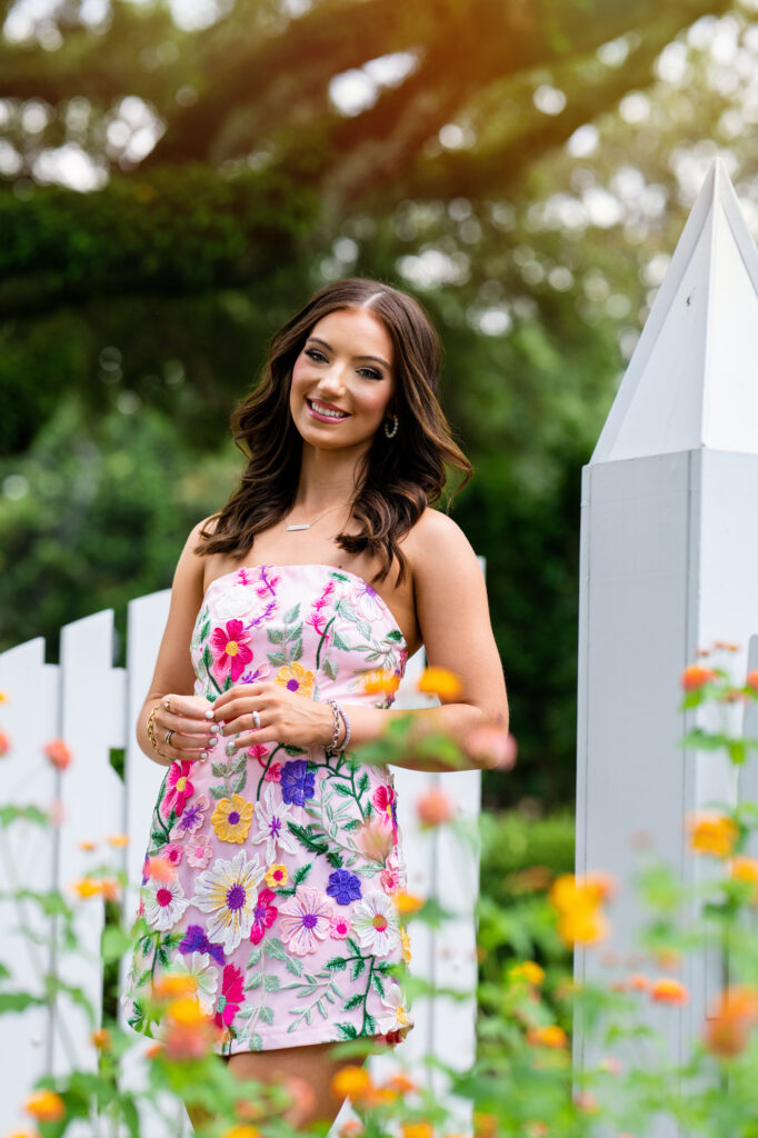 High school senior poses for her senior pictures in Tuscaloosa with Chris Landau Photography. She is wearing an embroidered floral dress on the Gorgas Museum grounds.
