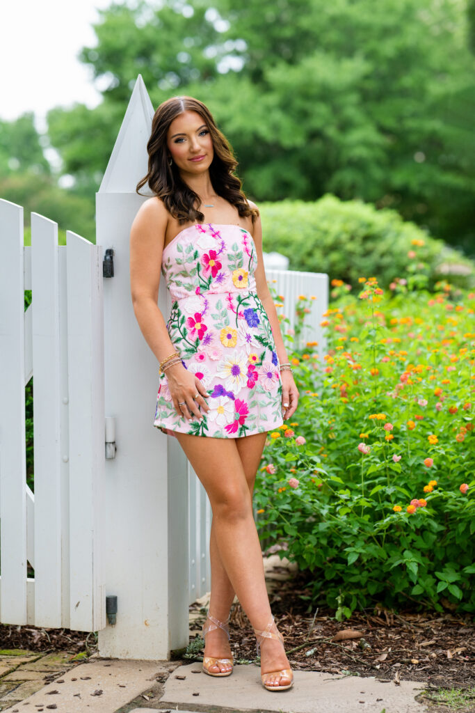 High school senior poses for her senior pictures in Tuscaloosa Alabama during her session with Chris Landau Photography. She is wearing an embroidered floral dress on the Gorgas Museum grounds.