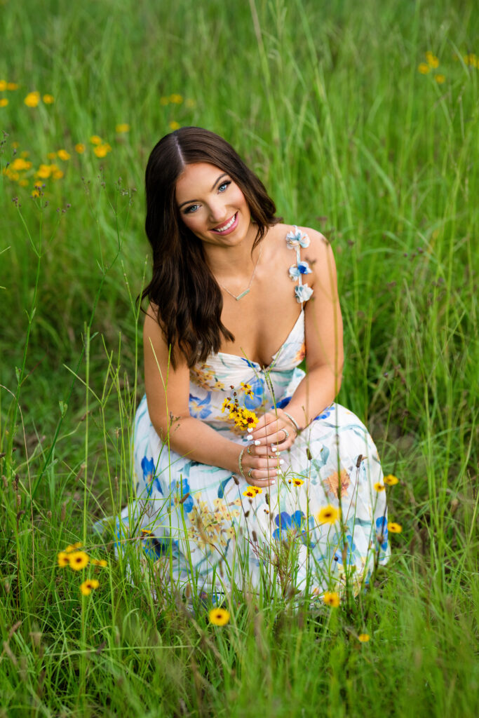 high school senior portrait in field of flowers tuscaloosa High school senior poses for her senior pictures in Tuscaloosa Alabama during her session with Chris Landau Photography. She is wearing a floral maxi-dress in a field of flowers while holding yellow flowers.
