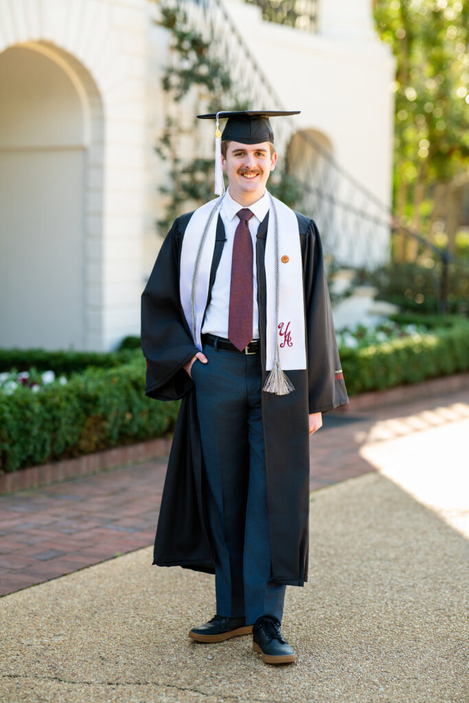 University of Alabama grad guy wearing his cap and gown and stole in front of President's Mansion for his graduation photos with Chris Landau Photography