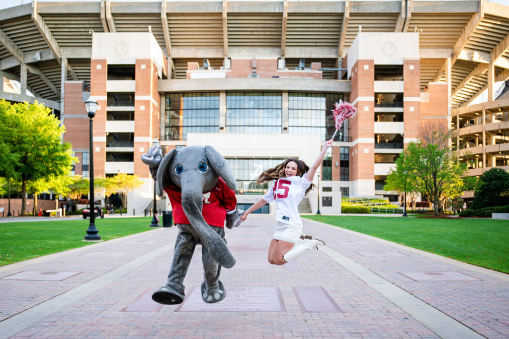Albama Mascot Big AL jumps in the air with Alabama graduate during her photoshoot with Chris landau Photography Alabama grad photographer.