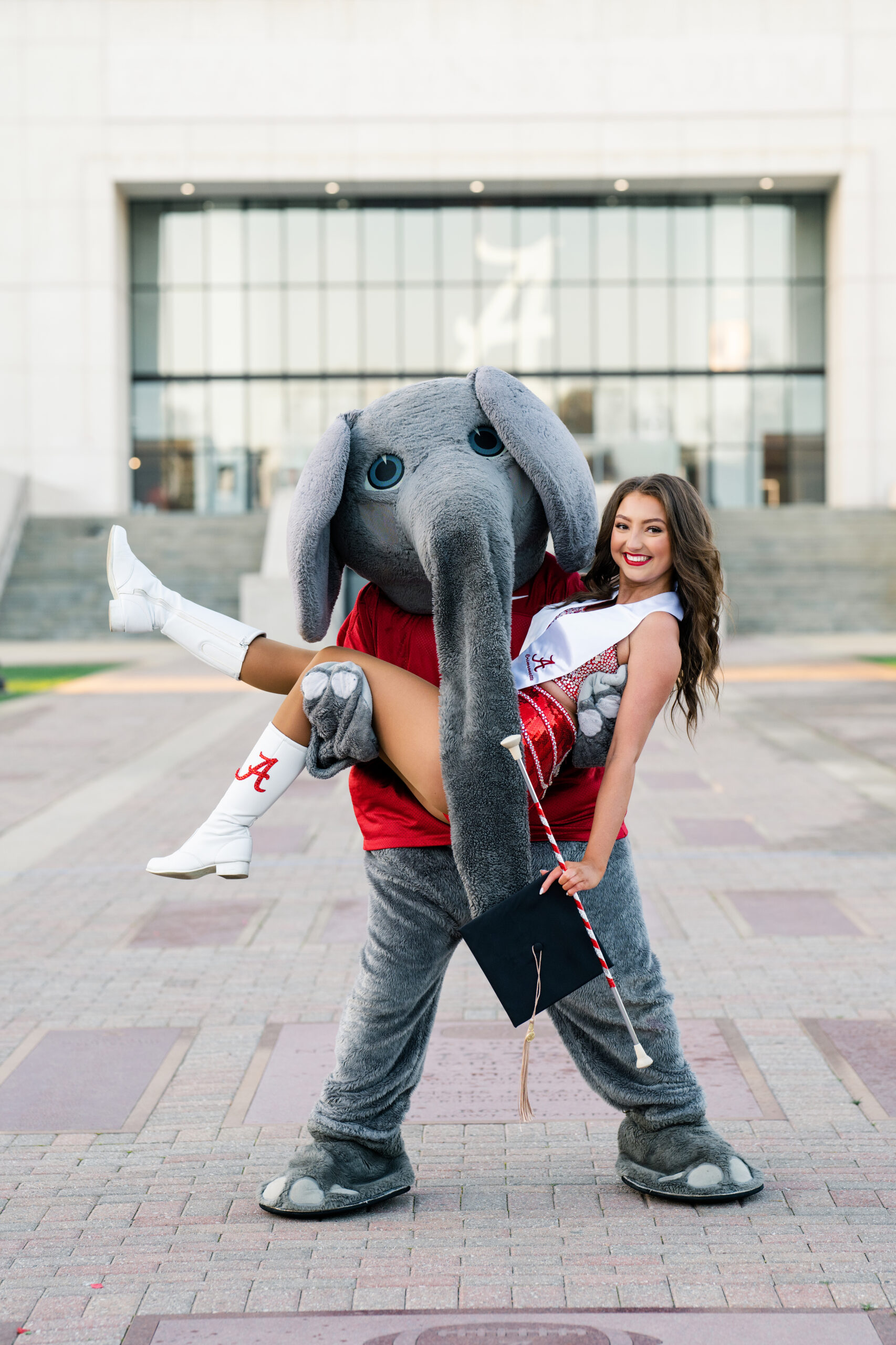 Big Al the Alabama mascot is holding a crimsonette in uniform for her graduation photoshoot
