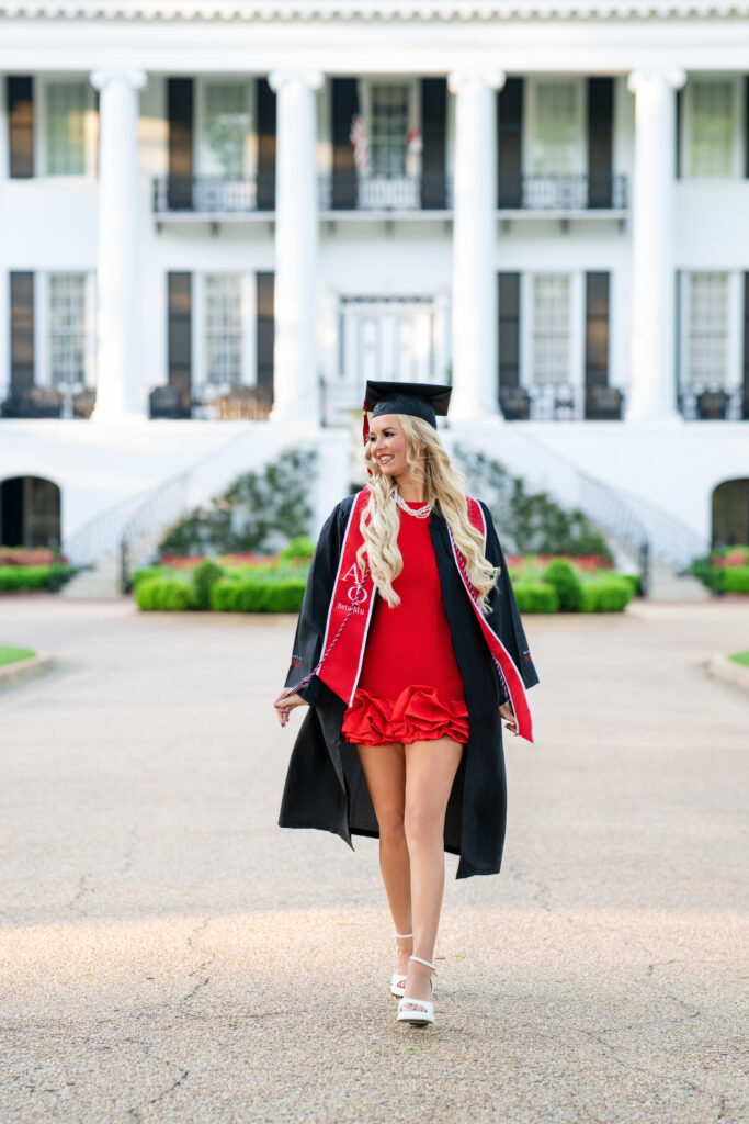 university of Alabama graduate walks in front of president's mansion for her grad photos with Chris Landau Photography
