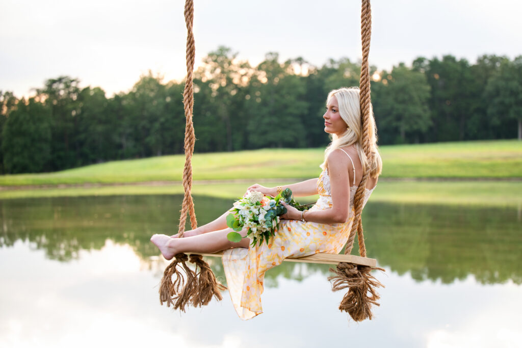High school senior girl on a rope swing over water with flowers in her lap