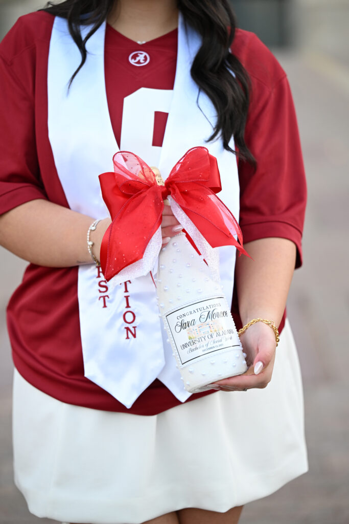 Alabama grad holds customized champagne bottle at her graduation photoshoot