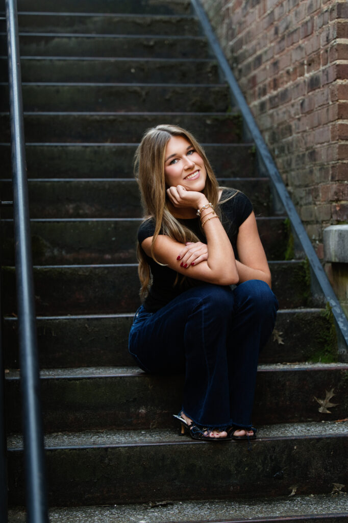 High school senior girl sits on stairs posing for senior photos with Chris Landau Photography. 