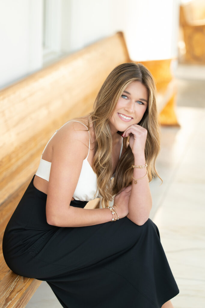 High school senior girl sits on bench smiling during her photoshoot with Chris Landau.