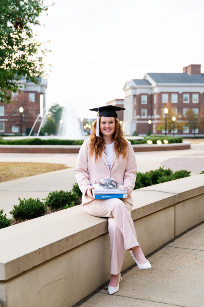 Bama grad holds books and goggles and wears her grad cap at Shelby Hall